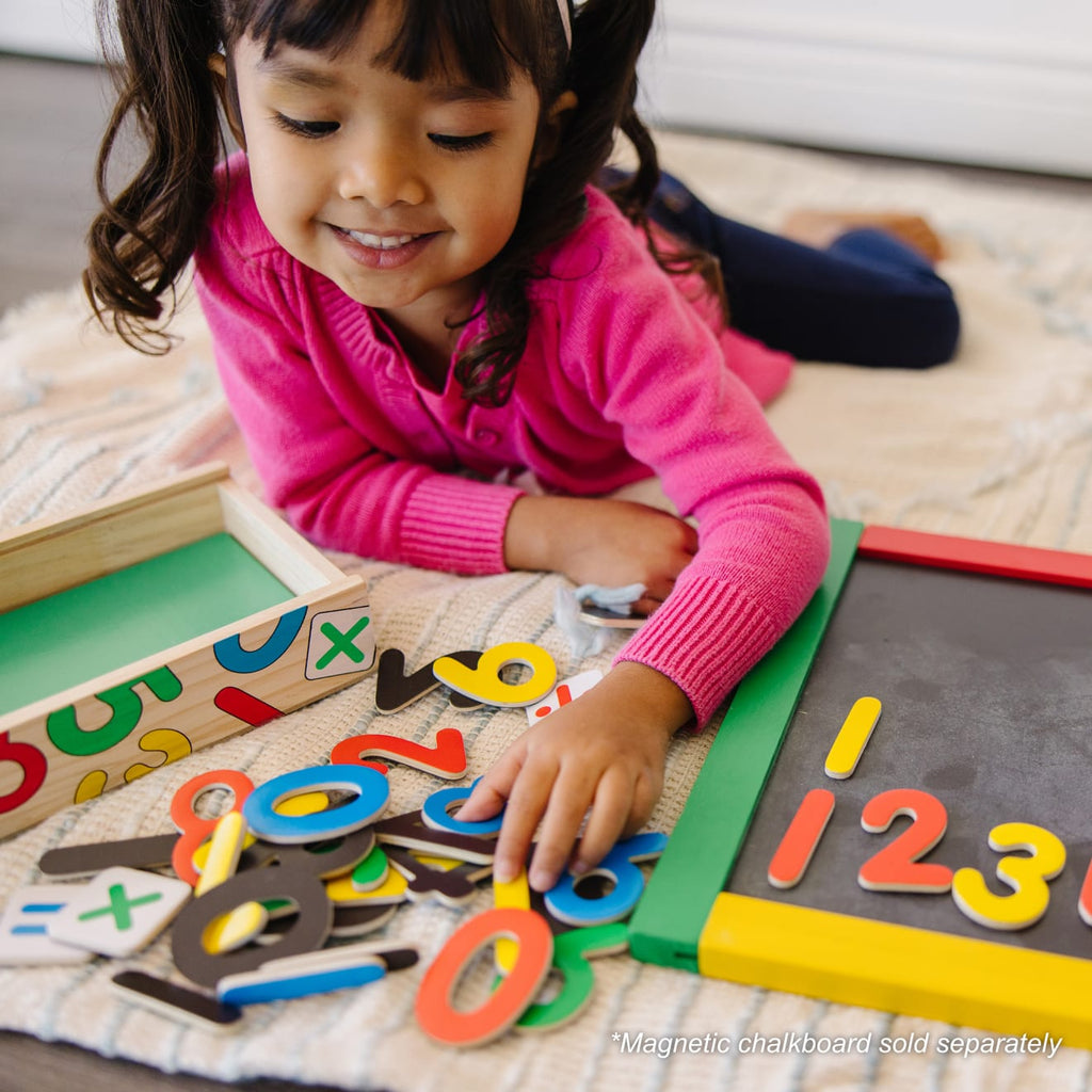 Niña jugando con números magnéticos de madera sobre una pizarra