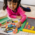 Niña jugando con números magnéticos de madera sobre una pizarra