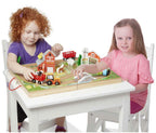 Dos niñas jugando con la granja de madera Take-Along Farm sobre una mesa