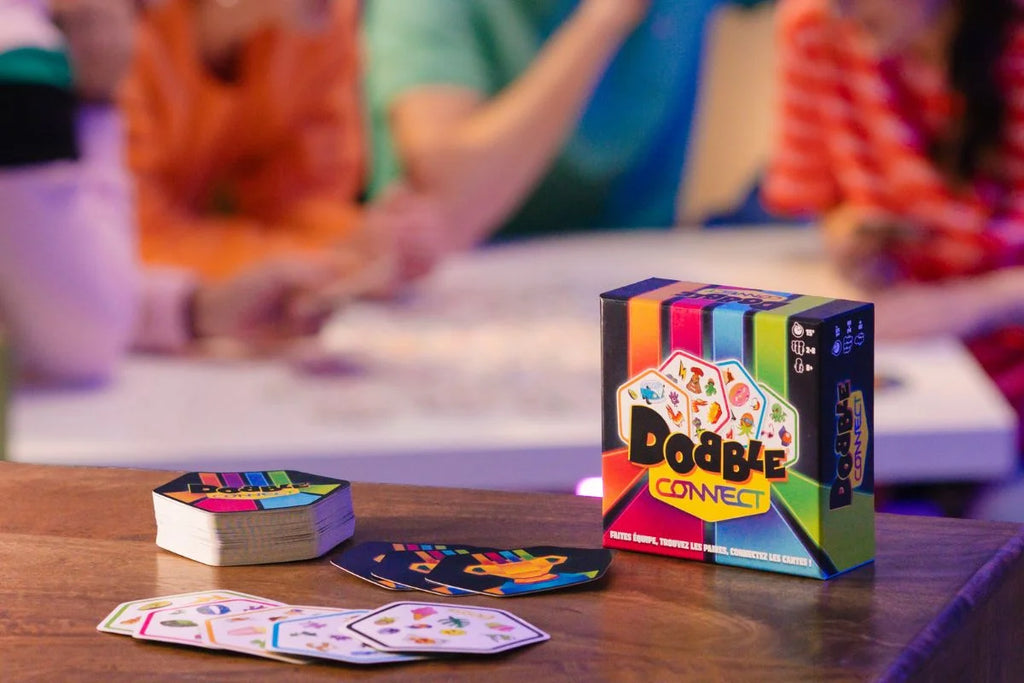 Caja de Dobble Connect con mazos de cartas de colores sobre la mesa