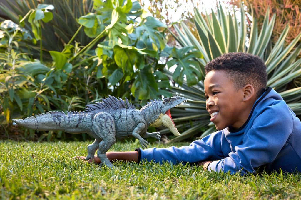 Niño jugando en el pasto con el Giganotosaurus Colossal Chomp