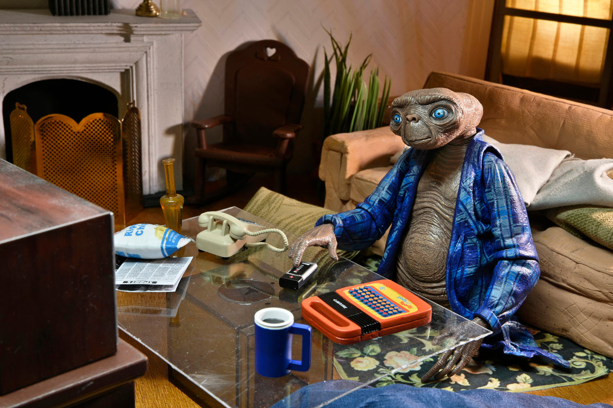 Figura NECA E.T. 40 aniversario sentada junto a una mesa con teléfono y Speak & Spell